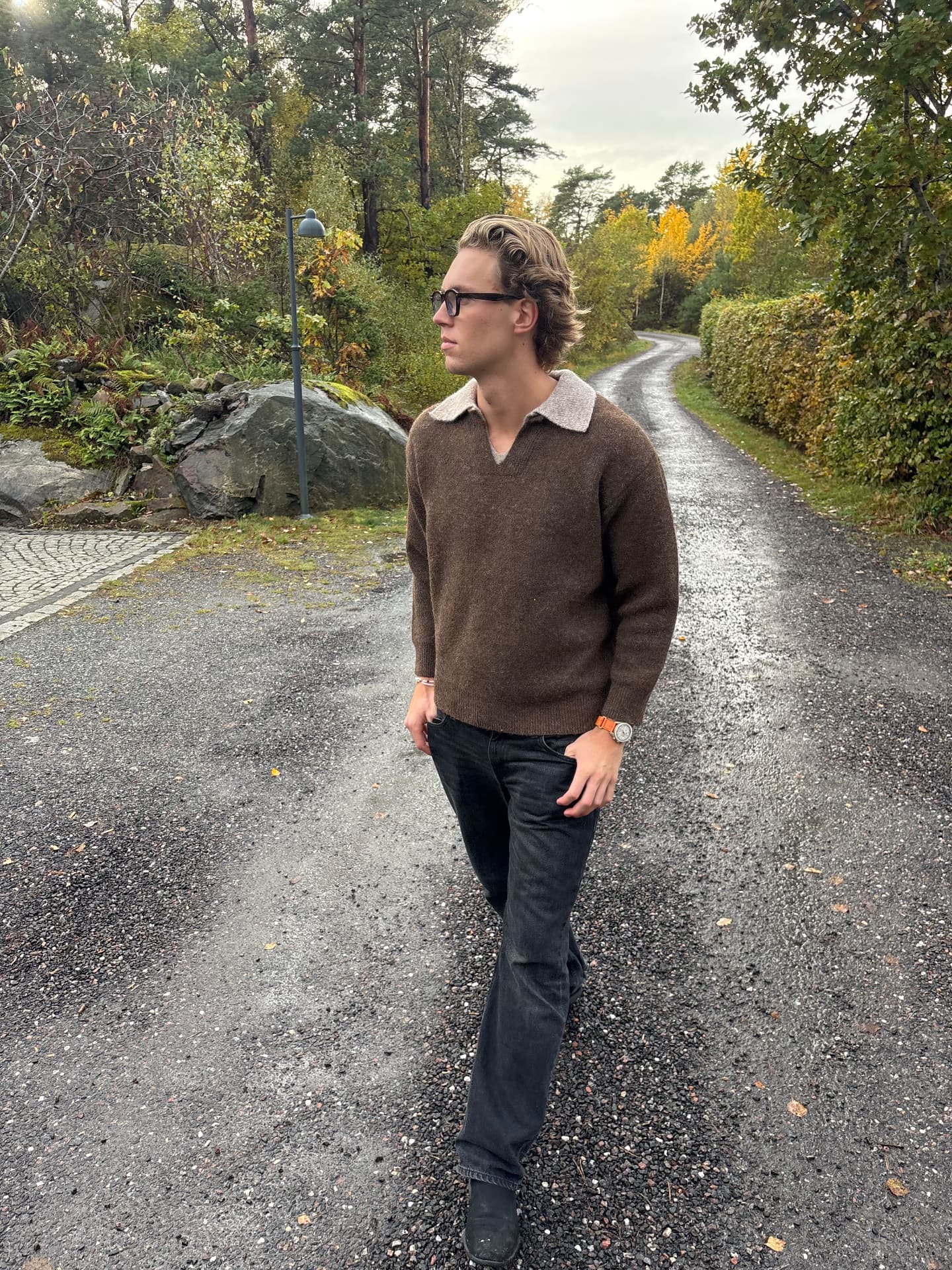 Man walking on a wet gravel road in the Swedish countryside wearing a brown knit sweater