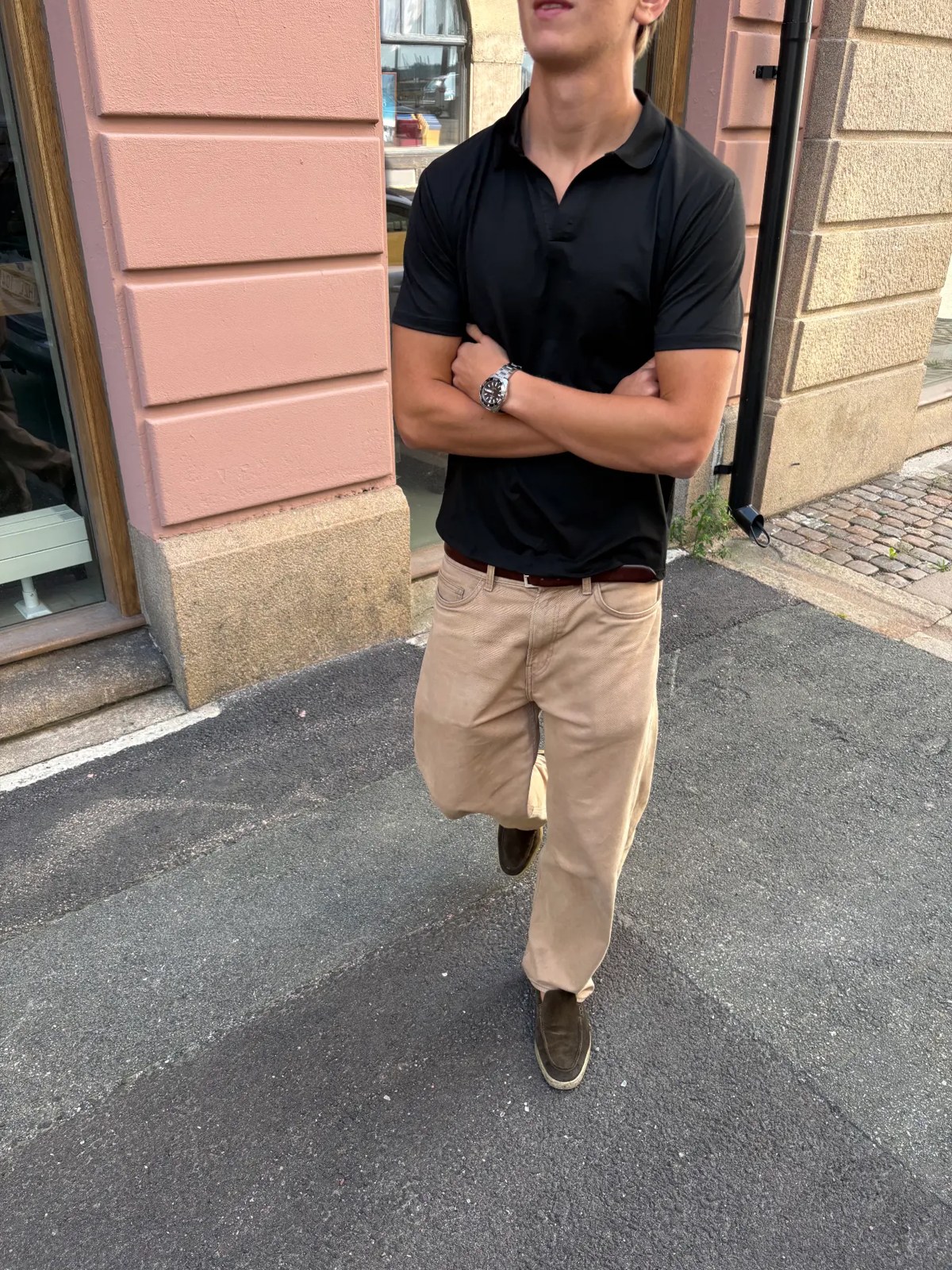 Model wearing a black polo t-shirt and beige trousers on a city street