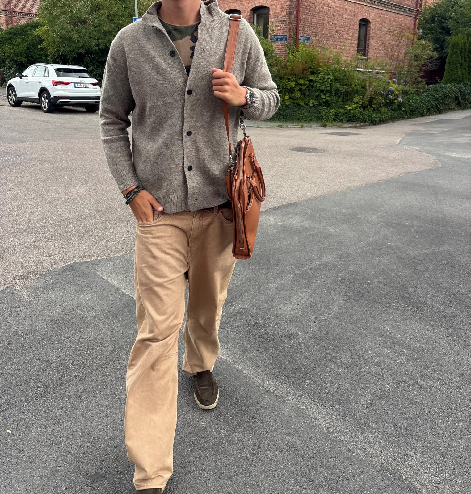 Man walking outdoors in a grey wool cardigan with tan trousers and a leather bag