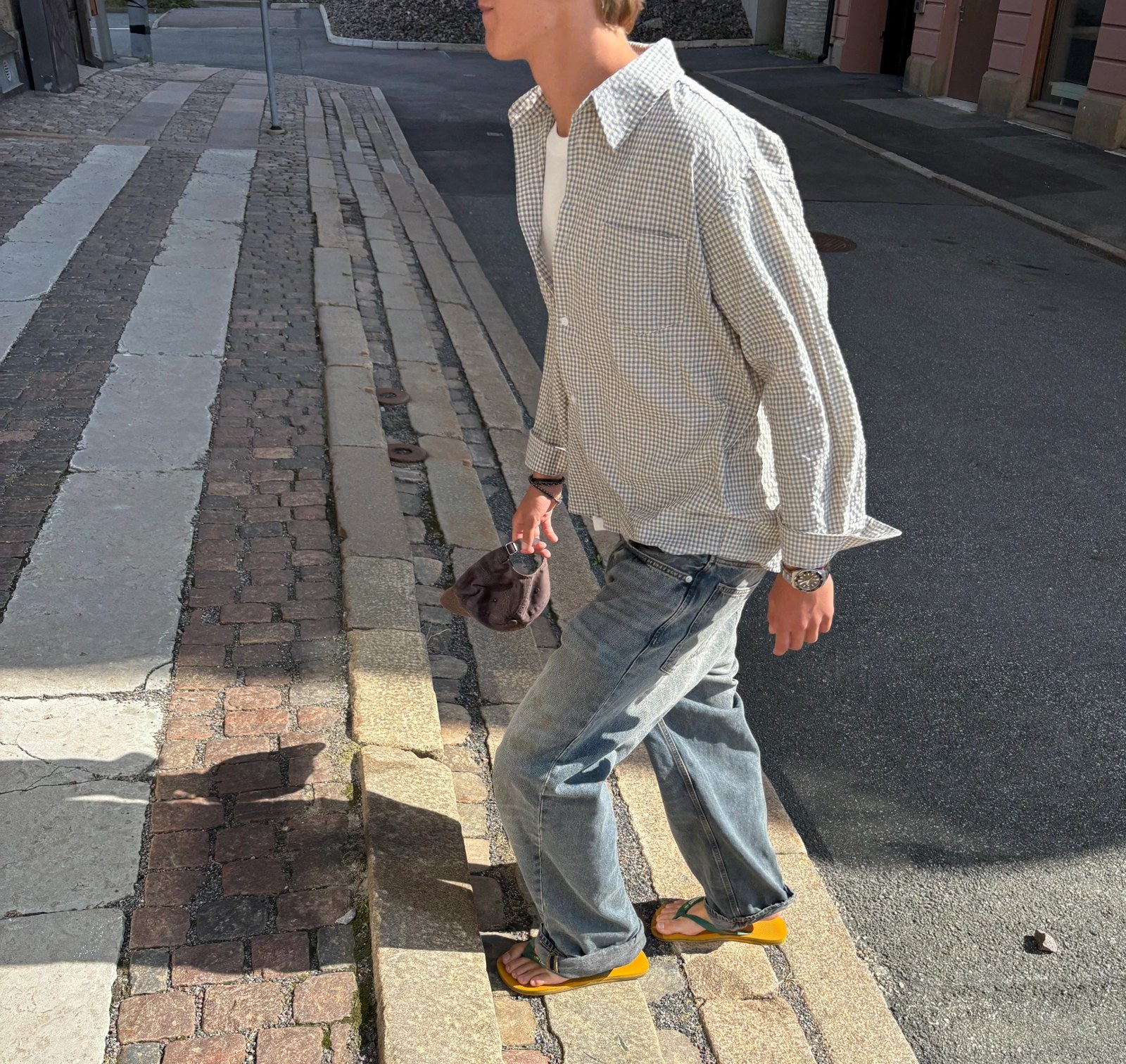 Model crossing a cobbled street in an oversized checked shirt and washed denim