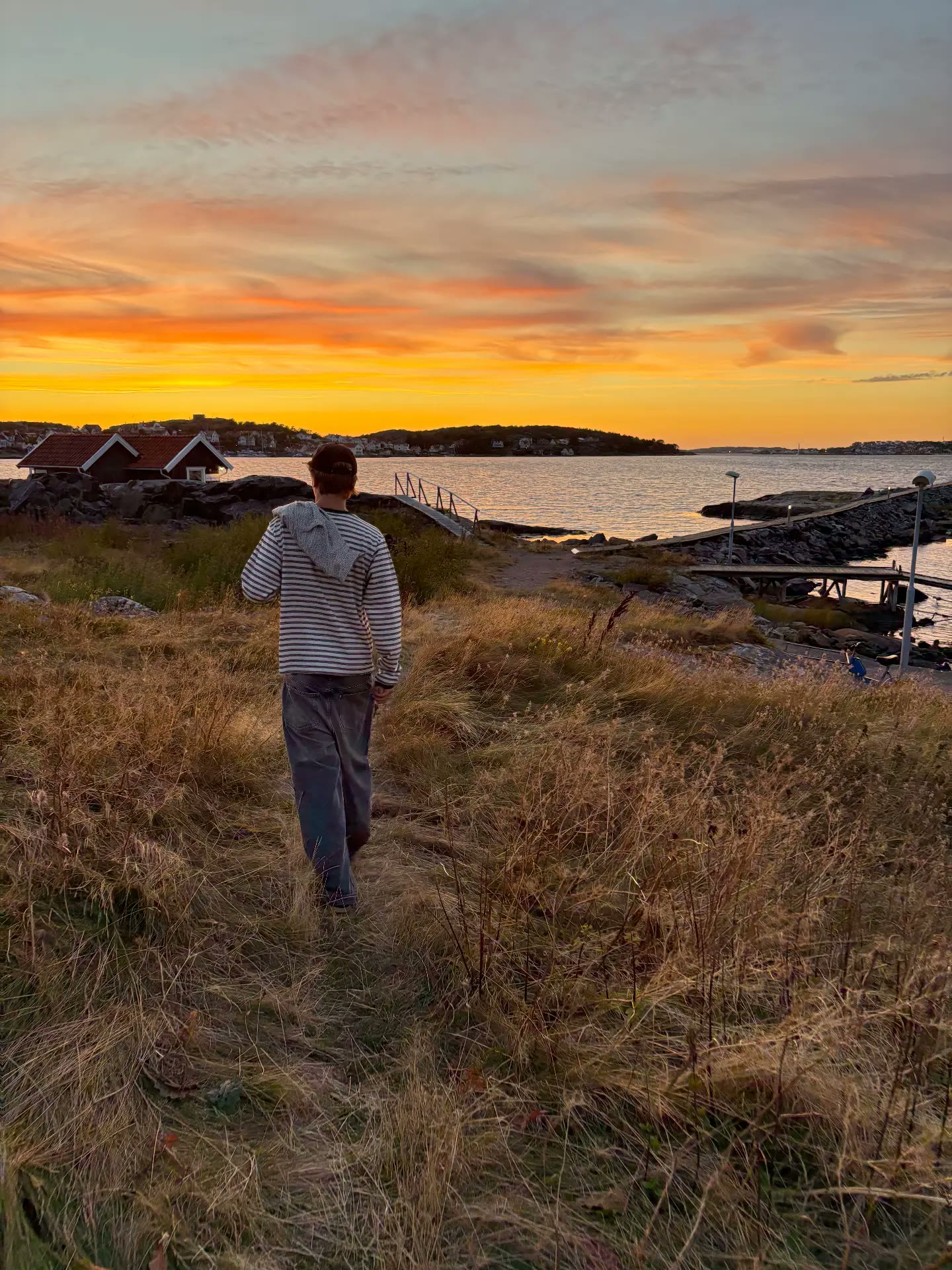 Model in a striped hooded sweater walking through coastal grass at sunset