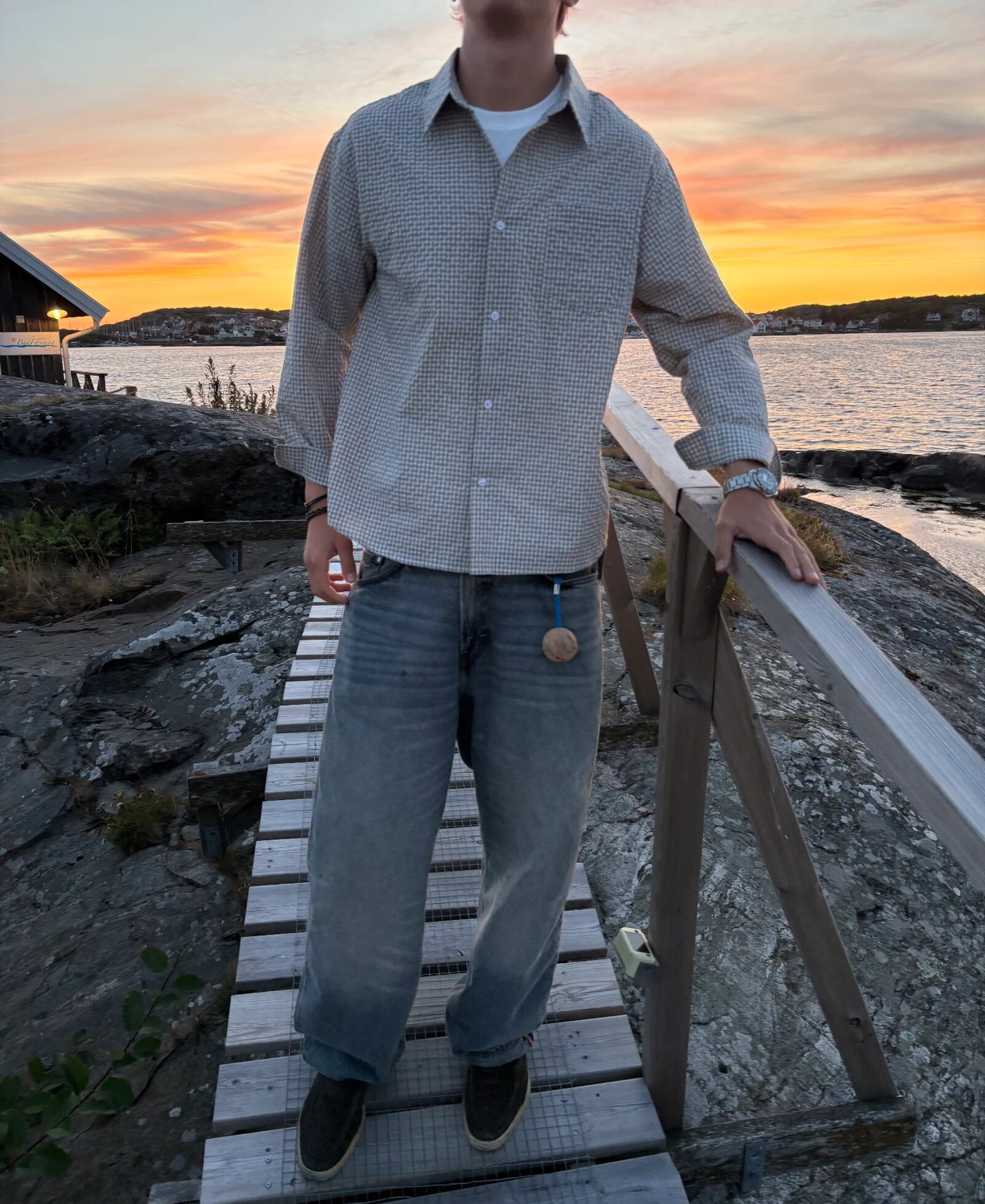 Model on a wooden jetty at sunset wearing a checked overshirt and washed denim